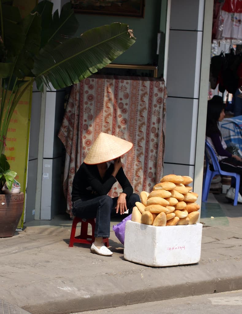 Bánh-Mì-Verkäuferin mit einem Stapel frischer Baguettes auf einer Straße in Hanoi
