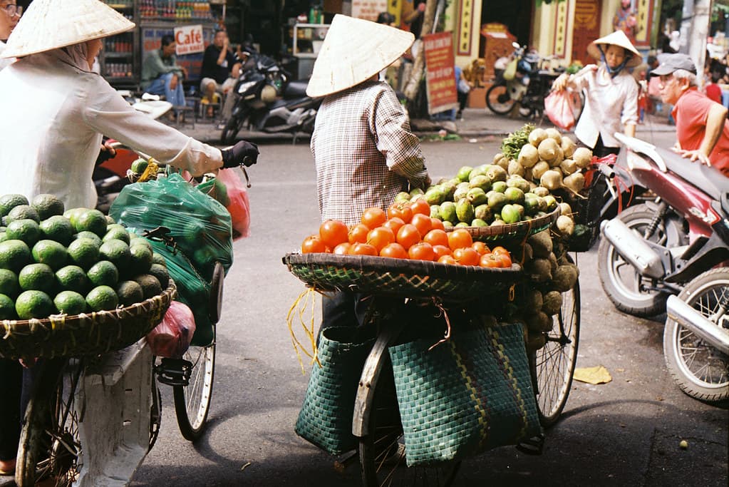 Straßenhändlerinnen mit Obstkörben auf Fahrrädern in der Altstadt von Hanoi